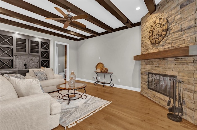 living room with baseboards, ceiling fan, wood finished floors, beamed ceiling, and a fireplace