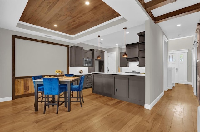 kitchen with a raised ceiling, light countertops, stainless steel microwave, and decorative light fixtures