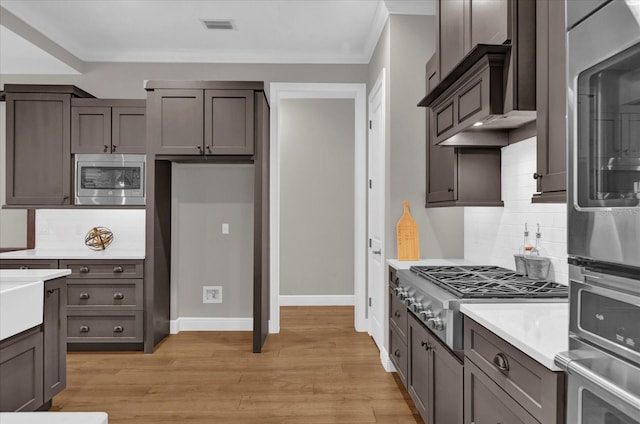 kitchen featuring light wood-style flooring, appliances with stainless steel finishes, light countertops, and crown molding