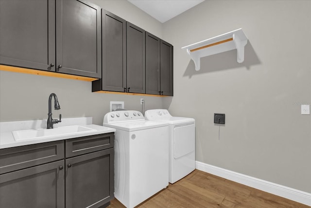 clothes washing area with washer and clothes dryer, light wood finished floors, cabinet space, a sink, and baseboards