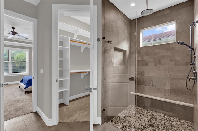 bathroom with a spacious closet, a tile shower, a wealth of natural light, and baseboards