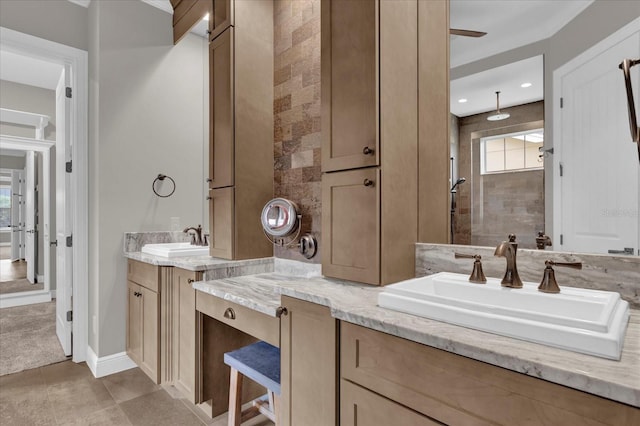 bathroom with a tile shower, two vanities, a sink, and baseboards