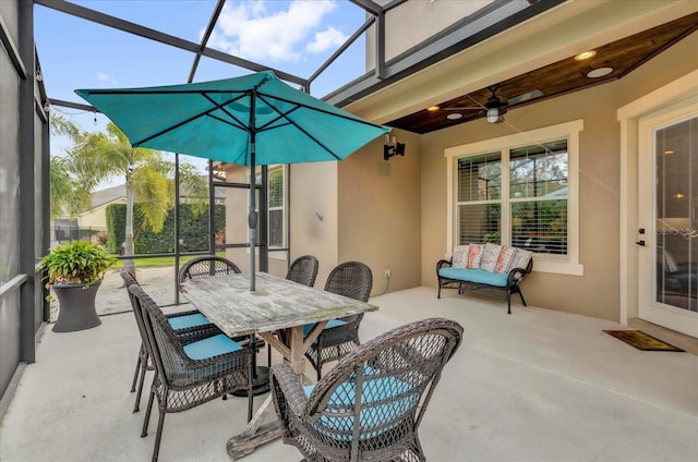 view of patio / terrace with glass enclosure, outdoor dining space, and a ceiling fan