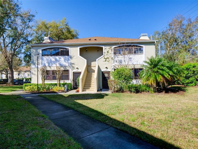 view of front of property featuring a front lawn, stairway, a chimney, and stucco siding