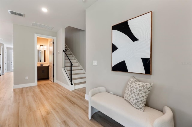 living area with stairs, light wood finished floors, visible vents, and baseboards