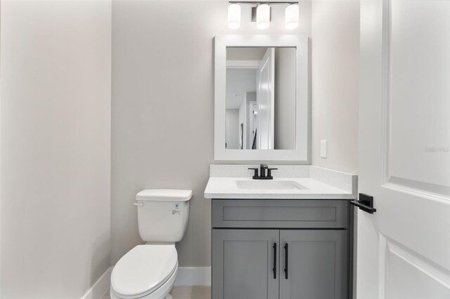 half bathroom featuring toilet, vanity, and baseboards