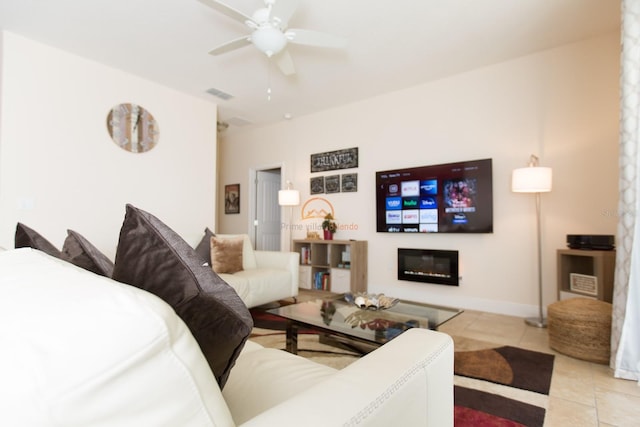 living room featuring light tile patterned floors, visible vents, a glass covered fireplace, ceiling fan, and baseboards