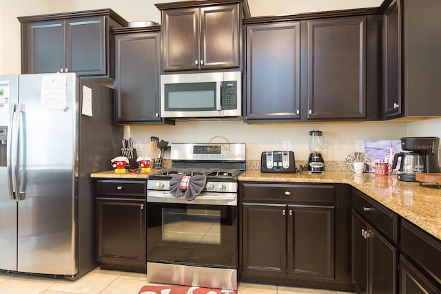 kitchen featuring light tile patterned floors, dark brown cabinets, appliances with stainless steel finishes, and light stone countertops