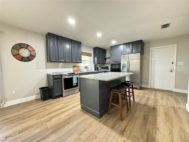 kitchen with visible vents, appliances with stainless steel finishes, light stone counters, a center island, and backsplash