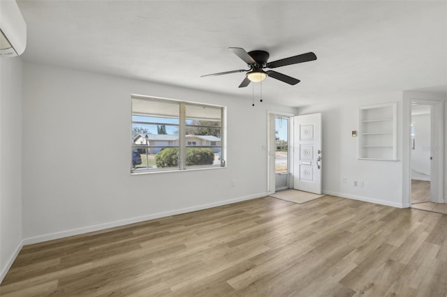 empty room with ceiling fan, built in features, baseboards, an AC wall unit, and light wood finished floors