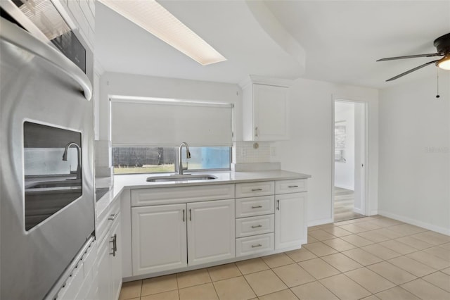 kitchen with white cabinets, a sink, light countertops, fridge, and backsplash