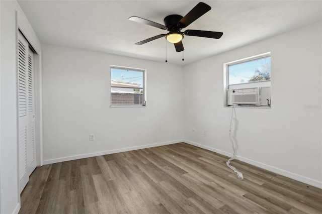 unfurnished bedroom featuring multiple windows, baseboards, cooling unit, and wood finished floors