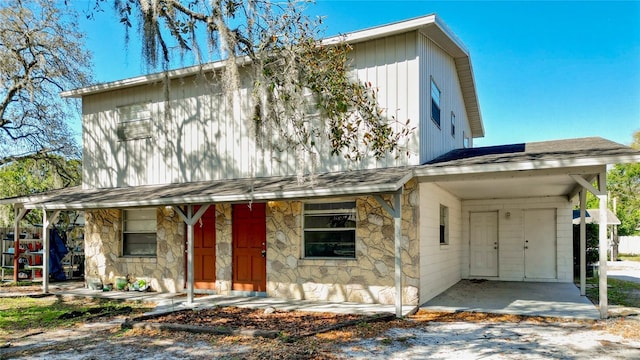 view of front of home featuring stone siding, a carport, roof with shingles, and driveway