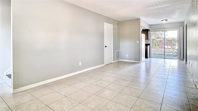 unfurnished room featuring light tile patterned floors, visible vents, a fireplace, and baseboards