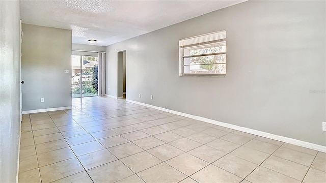 empty room featuring light tile patterned floors, baseboards, and a textured ceiling