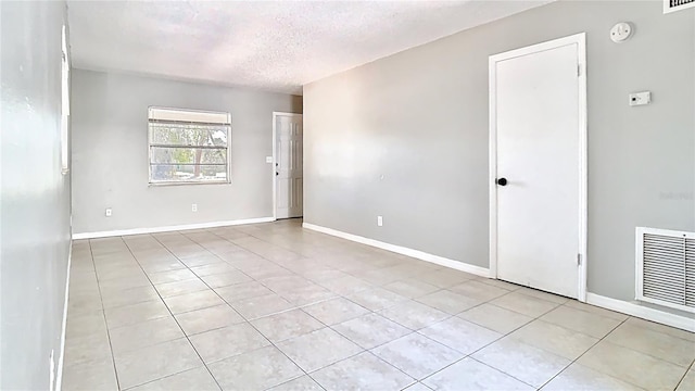 spare room featuring light tile patterned floors, visible vents, a textured ceiling, and baseboards