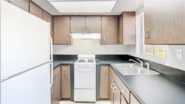 kitchen with white appliances, dark countertops, under cabinet range hood, and a sink