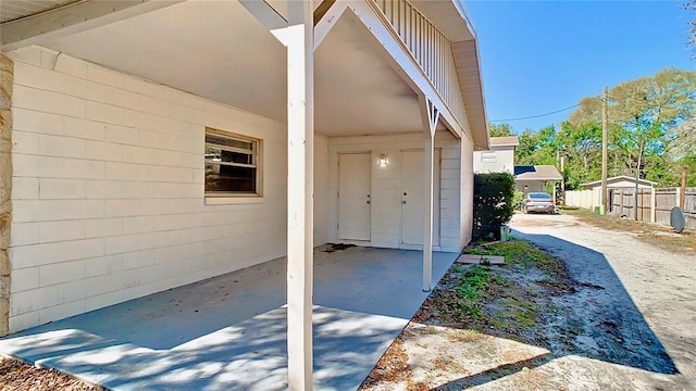 view of exterior entry with concrete block siding and fence