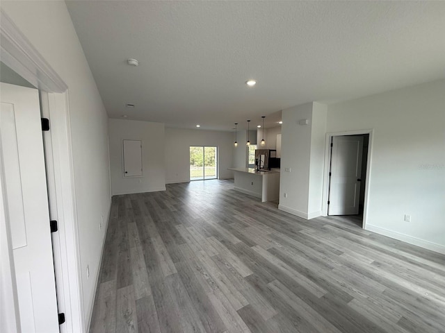 unfurnished living room featuring light wood-style flooring, baseboards, a textured ceiling, and recessed lighting