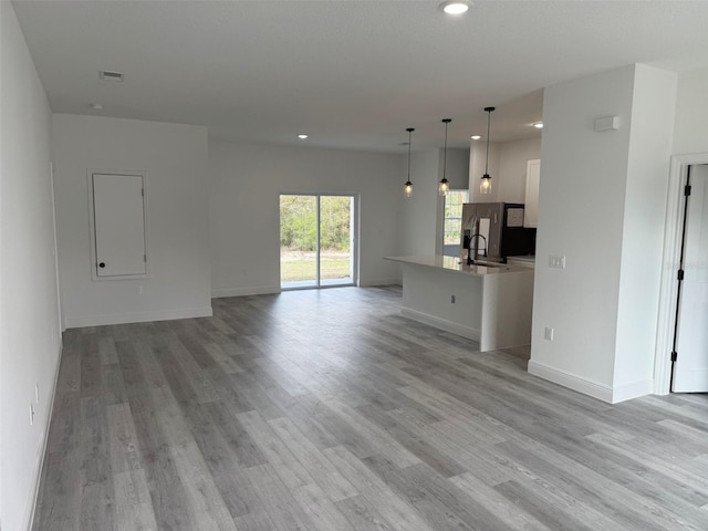 unfurnished living room with visible vents, baseboards, light wood-style flooring, a sink, and recessed lighting