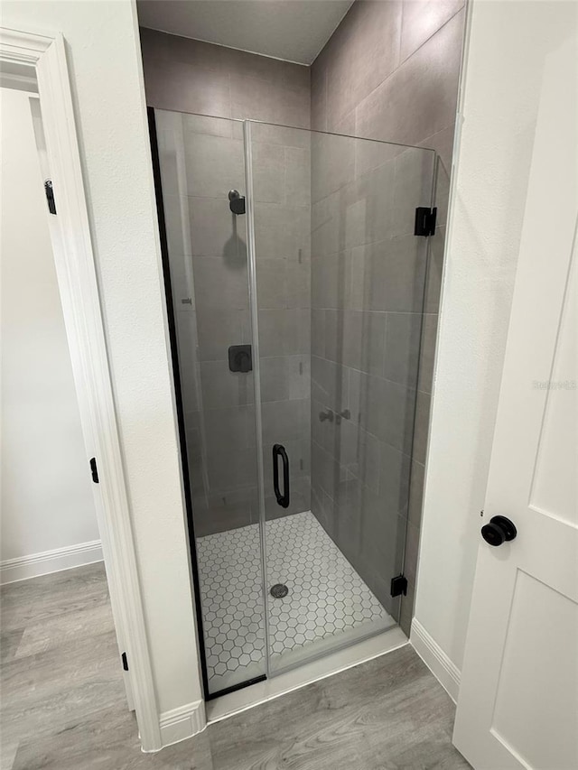 full bathroom with a shower stall, baseboards, and wood finished floors