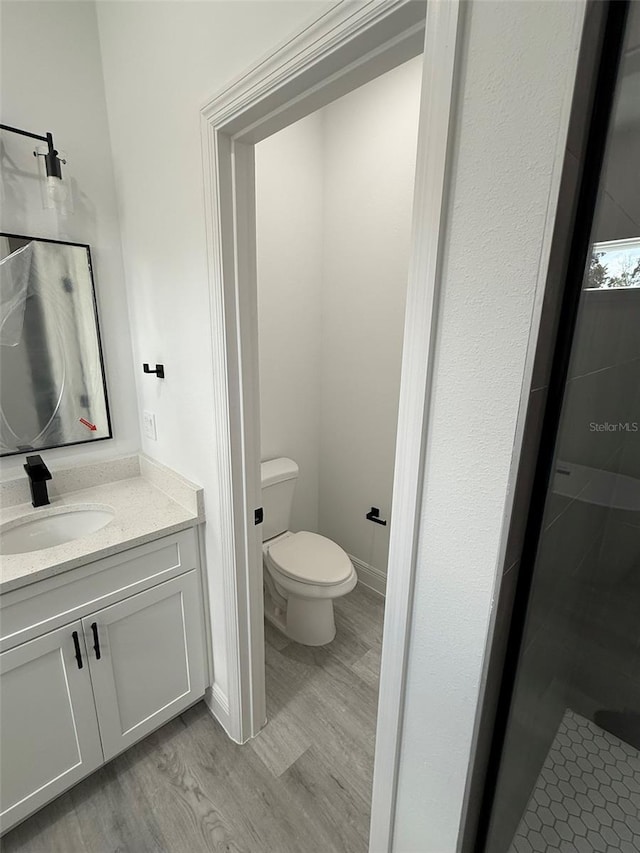 bathroom with toilet, wood finished floors, vanity, and baseboards