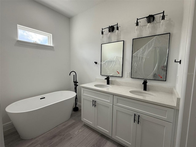 full bathroom featuring double vanity, a freestanding tub, a sink, and wood finished floors