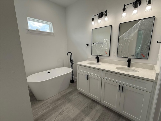 full bathroom with double vanity, a freestanding tub, a sink, and wood finished floors