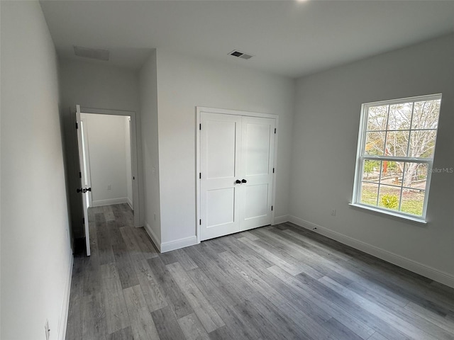 unfurnished bedroom featuring a closet, visible vents, baseboards, and wood finished floors