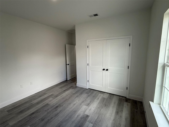 unfurnished bedroom featuring dark wood-style floors, a closet, visible vents, and baseboards