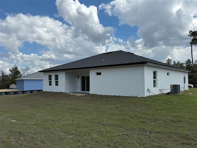 rear view of property with a yard, a shingled roof, cooling unit, and stucco siding