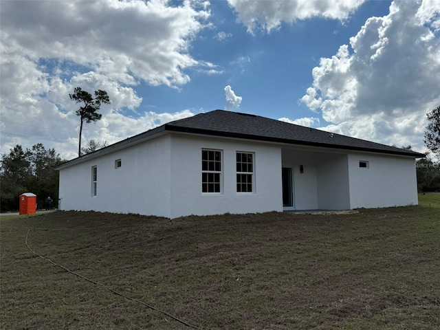 rear view of house featuring a lawn and stucco siding