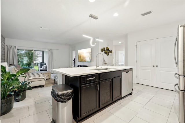 kitchen with pendant lighting, light countertops, appliances with stainless steel finishes, a kitchen island with sink, and a sink