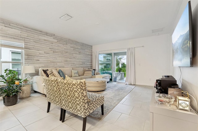 living room with light tile patterned floors, baseboards, visible vents, an accent wall, and wood walls