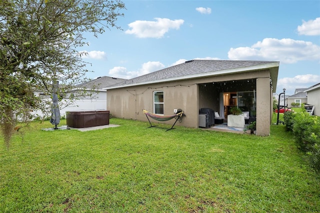 rear view of house with roof with shingles, a lawn, stucco siding, and a hot tub