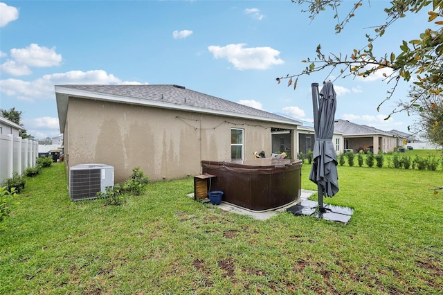 back of house featuring central AC unit, a lawn, stucco siding, and a hot tub