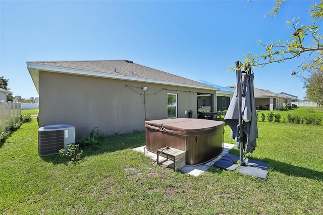 rear view of property featuring stucco siding, central AC, fence, a yard, and a hot tub