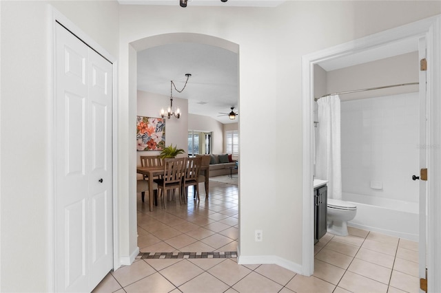 hallway featuring arched walkways, lofted ceiling, light tile patterned flooring, a chandelier, and baseboards