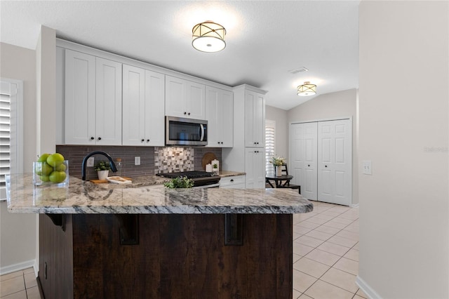 kitchen with light tile patterned floors, appliances with stainless steel finishes, vaulted ceiling, a sink, and a peninsula