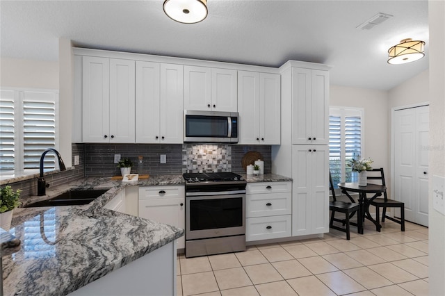 kitchen featuring light tile patterned floors, tasteful backsplash, stainless steel appliances, white cabinetry, and a sink