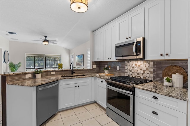 kitchen with light tile patterned floors, decorative backsplash, a peninsula, stainless steel appliances, and a sink