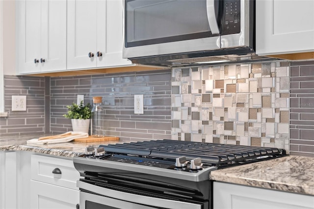 kitchen featuring stainless steel appliances, white cabinetry, light stone counters, and decorative backsplash