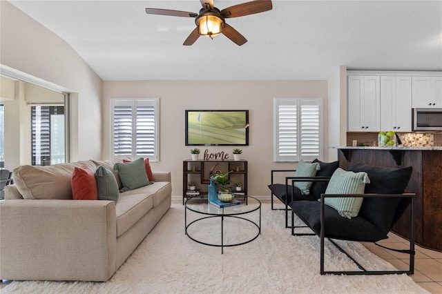 living area featuring a ceiling fan, lofted ceiling, baseboards, and light tile patterned floors