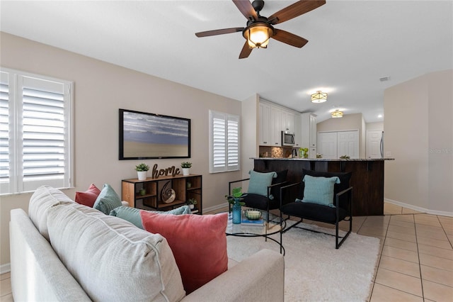 living room with lofted ceiling, ceiling fan, baseboards, and light tile patterned floors