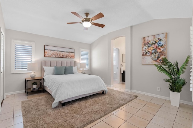 bedroom featuring lofted ceiling, light tile patterned floors, baseboards, and arched walkways