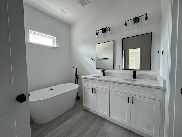 full bath featuring visible vents, a sink, a freestanding bath, and double vanity