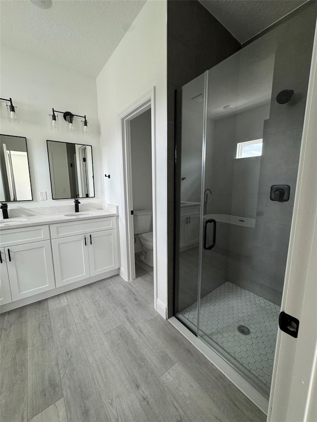 full bathroom with a stall shower, toilet, wood finished floors, a textured ceiling, and a sink