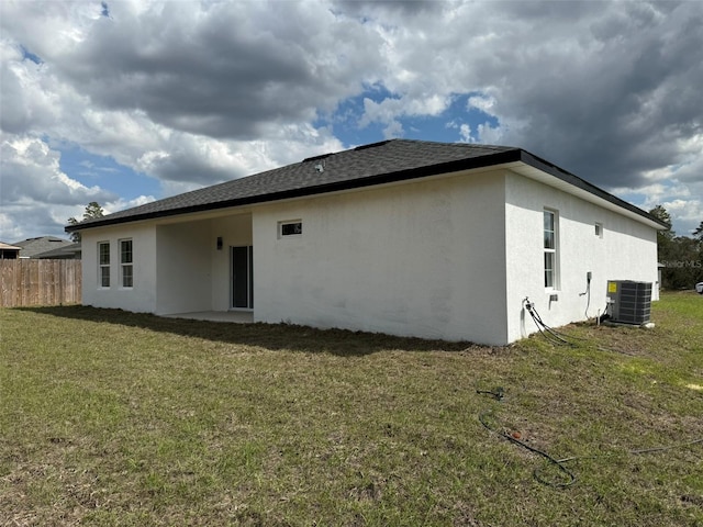 rear view of house featuring a shingled roof, fence, cooling unit, a yard, and stucco siding