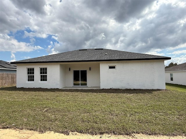 rear view of property featuring roof with shingles, a lawn, fence, and stucco siding