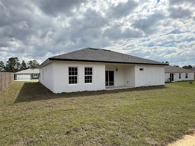 back of house with a shingled roof, a lawn, a detached garage, and stucco siding